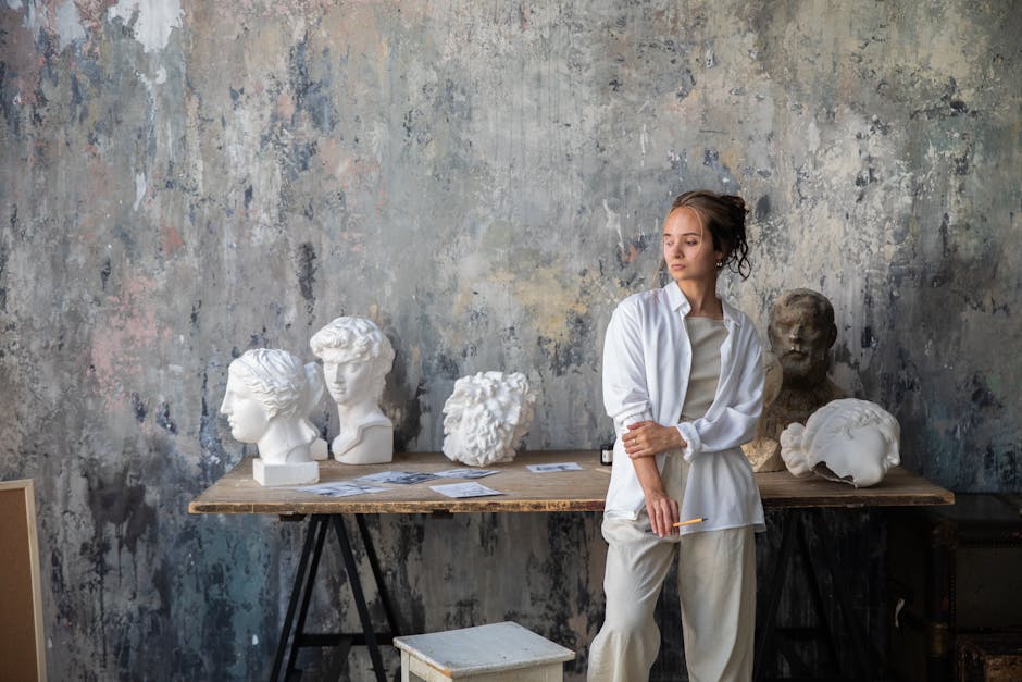 Artist in a studio surrounded by classical sculptures and artworks.