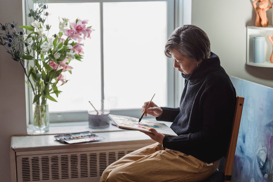 A woman artist painting near a window with flowers, showcasing her creativity indoors.